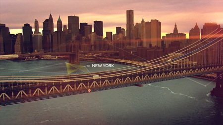 A suspension bridge spans a river in front of a dense skyline of skyscrapers during sunset.