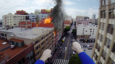 A high-angle view of thick black smoke and orange flames rising from a building on a city street.