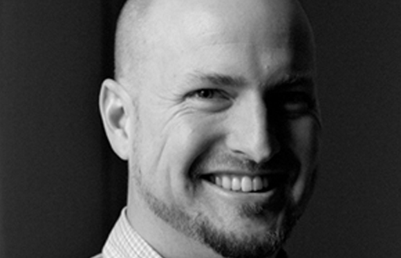 Black and white close-up portrait of a bald man with a goatee smiling.