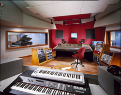 A professional recording studio featuring a large mixing console, red walls, and electronic keyboards.