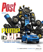 A blue car beneath a large robot-like structure constructed from numerous audio speakers and electronic components.