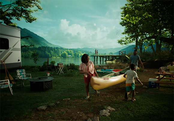 People carry a yellow canoe near a campsite by a lake with mountains in the background.