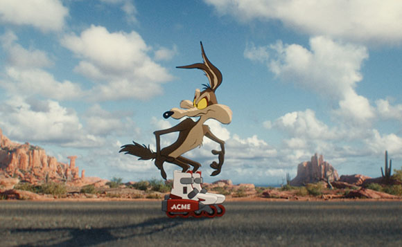 A cartoon coyote wearing white roller skates with red wheels, standing on a road in a desert landscape.