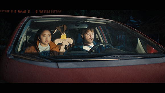 A man and a woman sit in a car at night next to a large cartoon rabbit character.