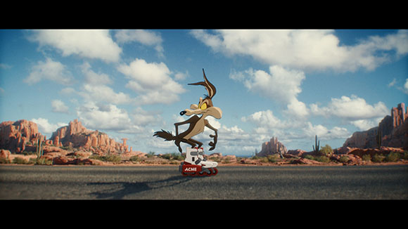 Cartoon coyote on white ACME roller skates in a sunny desert with mountains and clouds.