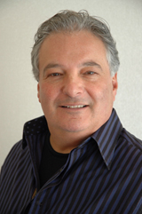 A smiling middle-aged man with graying hair wearing a dark blue striped button-down shirt.