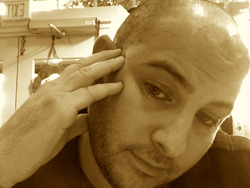 A sepia-toned close-up of a man resting his hand against his temple with a somber expression.