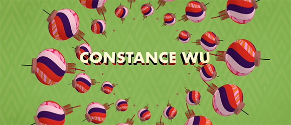 The name Constance Wu in bold white letters over floating colorful patterned spheres on a green background.