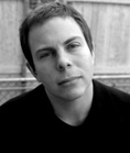 Black and white close-up portrait of a man looking directly at the camera.