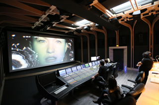 A large screen displays a close-up of a face in a dark professional post-production studio.
