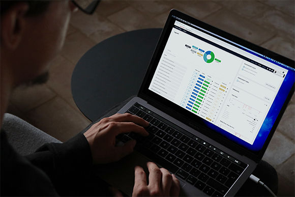 A person's hands typing on a laptop showing a dashboard with charts and data tables.