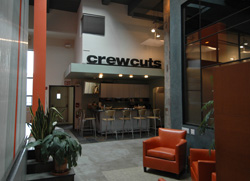 A modern salon lobby with orange armchairs, potted plants, and a service counter under a Crewcuts sign.