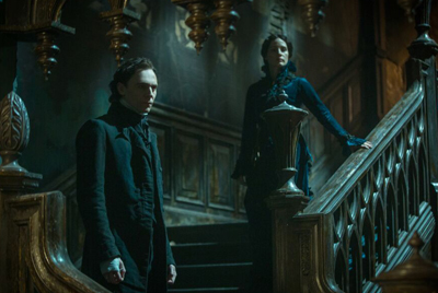 A man in a dark coat and a woman in a dark dress stand on a grand, dimly lit wooden staircase.