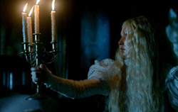 A woman with long blonde hair holds a four-candle candelabra in a dimly lit room.