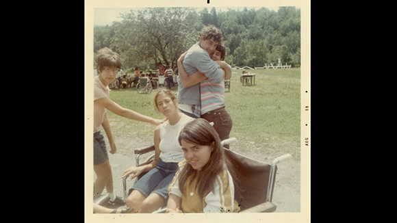 A group of five teenagers posing for a photo in a grassy field with trees in the background.