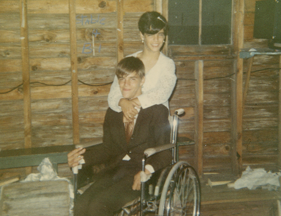 A person in a white shirt embraces a person sitting in a wheelchair.