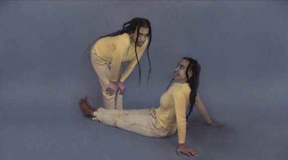 Two people in matching yellow long-sleeve shirts and pants posing on a solid gray floor.