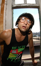 A man wearing a black helmet, large glasses, and a black tank top leans against a window frame.