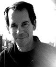 Black and white portrait of a man with dark hair smiling against a bright background.
