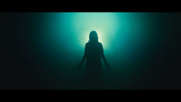 Silhouette of a person standing centered against a bright teal, misty light.