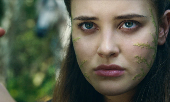 Close-up of a woman with green vine-like markings on her cheeks and a serious expression.