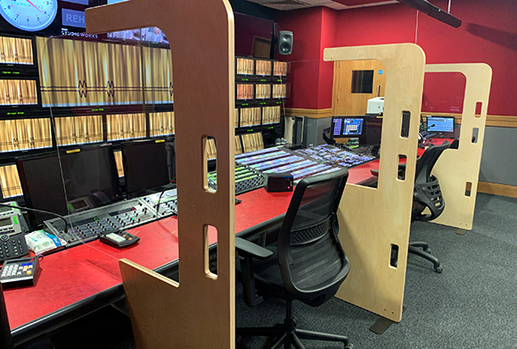 A radio studio featuring mixing consoles, computer monitors, and wooden acoustic partitions.