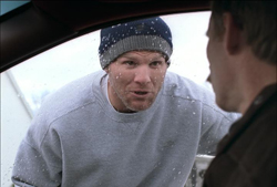 A man wearing a grey sweatshirt and a blue beanie looks toward a person in profile.