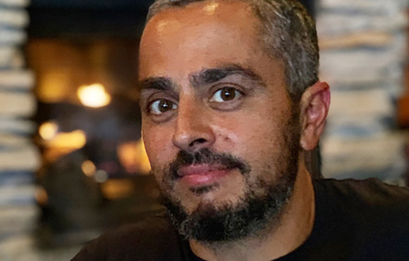 A man with short salt-and-pepper hair and a beard looking forward against a blurred background.