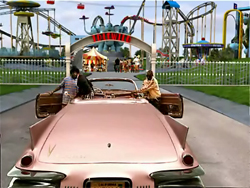 A pink vintage convertible parked on a path leading toward an amusement park entrance.