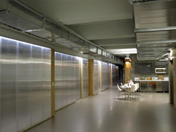 A wide hallway with large, silver metallic wall panels and exposed industrial ceiling ductwork.
