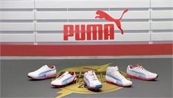 Puma logo on a white wall above five different white and blue athletic shoes on a gray floor.