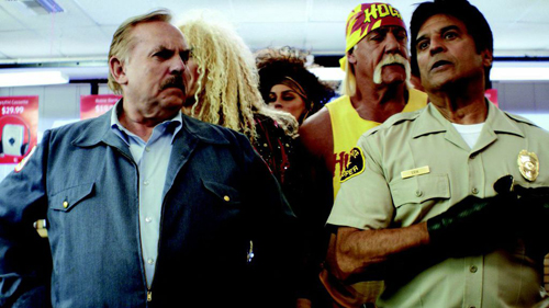 A group of people, including a man in a blue jacket and a man in a tan uniform, stand in a brightly lit room.