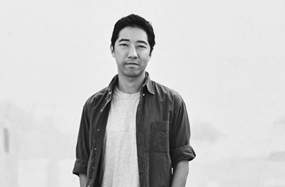 Black and white portrait of a man wearing a light t-shirt under a dark button-down shirt.