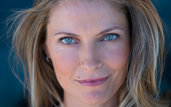 Close-up portrait of a woman with blonde hair and blue eyes looking directly at the camera.
