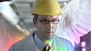 A man in a yellow hard hat, glasses, and a light blue shirt with large white feathered wings.