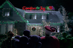 A house at night decorated with green lights and a red sign reading 'Comfort & Joy'.