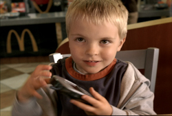 A young blonde boy smiling while holding a small dark object in his hands at a restaurant.