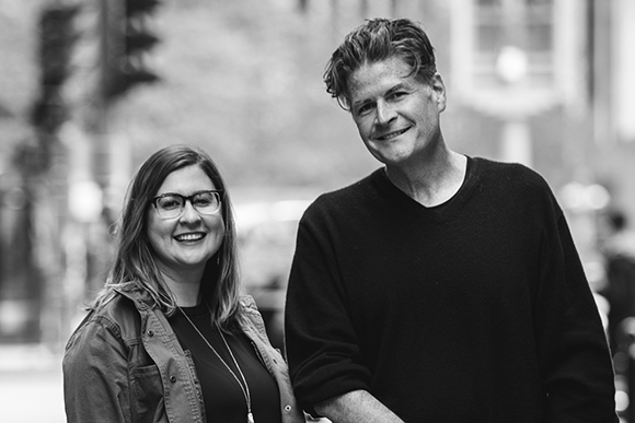 A smiling man and woman standing together in a black and white outdoor portrait.