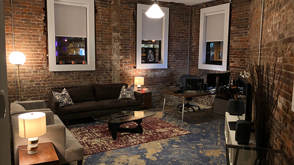A living room with exposed brick walls, a dark sofa, a coffee table, and a desk with a computer.