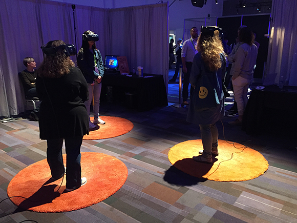 Several people wearing VR headsets stand on circular orange mats in a dark event space.