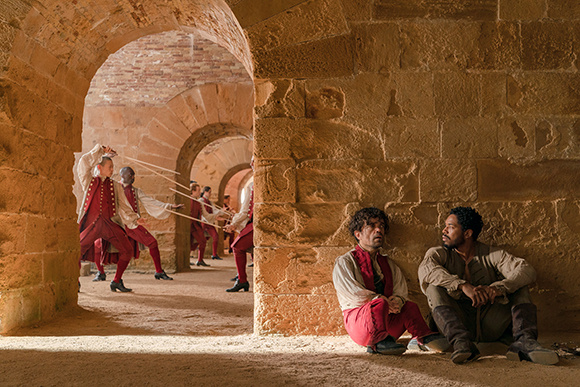 People in historical red and white clothing in a stone arched hallway.