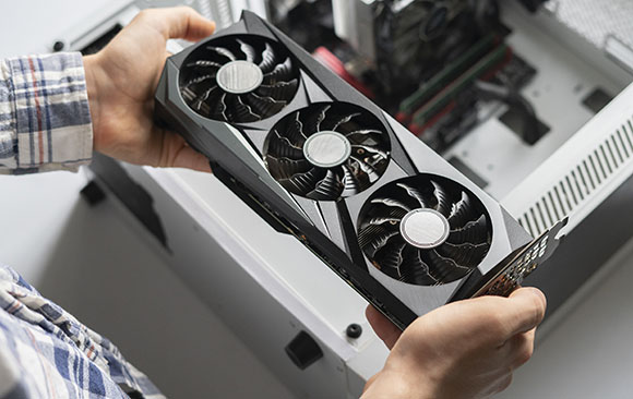 Hands holding a black triple-fan graphics card above an open white computer tower.