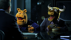 Two animal puppets in business suits sit at a dark table across from a man in a suit.