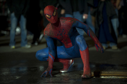 A person in a red and blue Spider-Man superhero suit crouches on a dark, wet street.