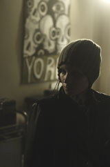 A person wearing a dark beanie and jacket stands in a dimly lit room near a skull poster.