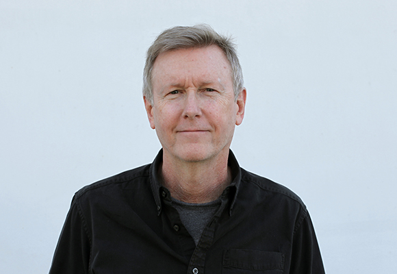 A middle-aged man with short graying hair wearing a black button-down shirt against a white background.