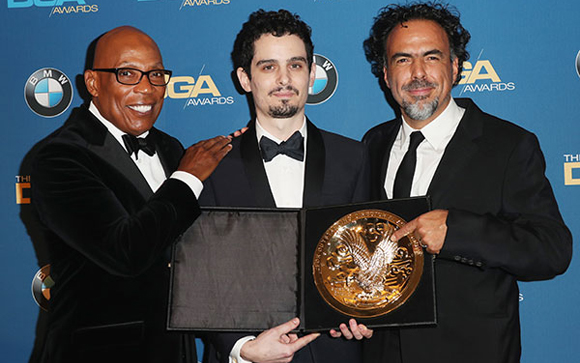 Three men in formal attire pose together, holding an open award box with a gold emblem.