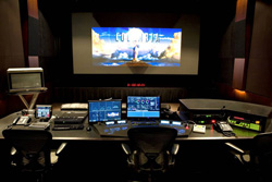 A dark control room with multiple monitors, a large projection screen, and professional editing equipment.