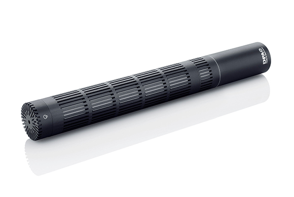 A long, black DPA cylindrical microphone with a slotted grille, angled on a white reflective surface.