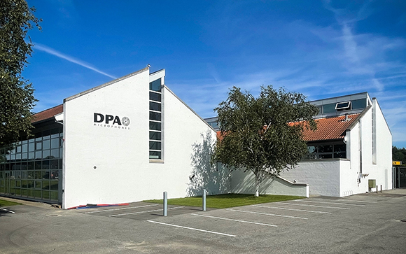 A white modern building with the DPA Microphones logo under a clear blue sky.
